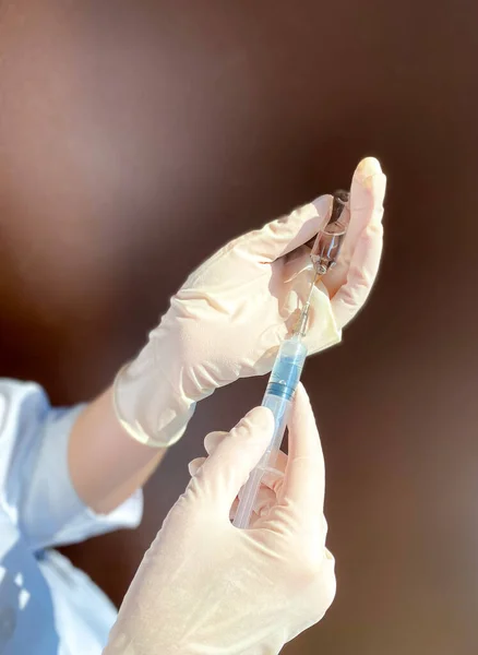 A fair-skinned woman doctor / medical worker in a white coat and disposable gloves holds an open ampoule with a medicine and a syringe in her hands.Free space.