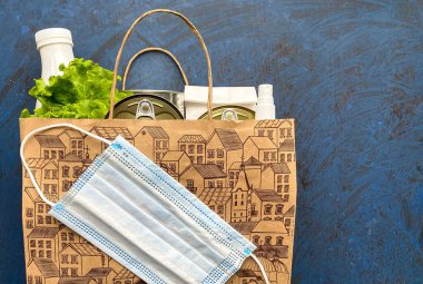 Paper bag with food, antiseptic and medical mask on a blue background. Food delivery, donation. Free space. clipart