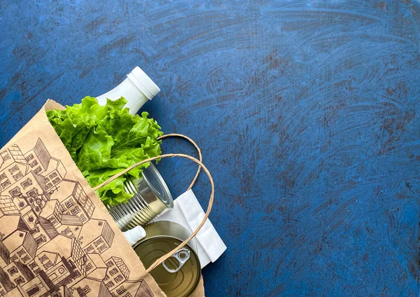 Paper bag with food, antiseptic and medical mask on a blue background. Food delivery, donation. Free space.