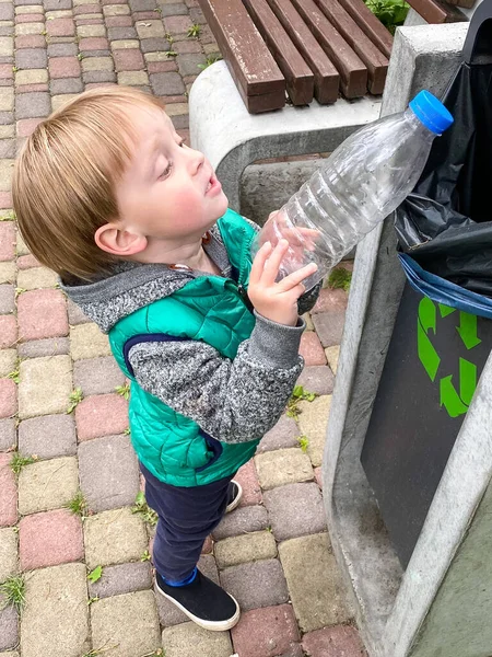 Açık tenli küçük bir çocuk plastik bir şişeyi çöp kutusuna atıyor..