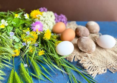 Mavi soyut bir zemin üzerinde renkli yabani çiçeklerle süslü Paskalya yumurtaları..