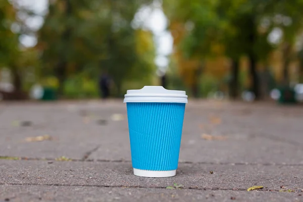 En blå kaffekopp i papper står på asfalten i höstens stadspark — Stockfoto