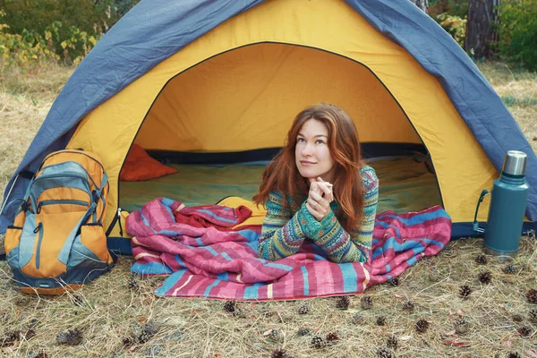 Pretty young redhead girl looking up, lying in yellow grey tent, relaxing, enjoying nature in autumn forest. ストックフォト