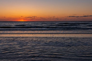 Karadeniz 'de gün batımında muhteşem bir manzara ve üzerinde muhteşem bir güneş ışığı olan turuncu gökyüzü arka plan olarak sakin dalgaların üzerinde. Sahilde muhteşem bir yaz gün batımı manzarası. Rus doğası, Soçi.