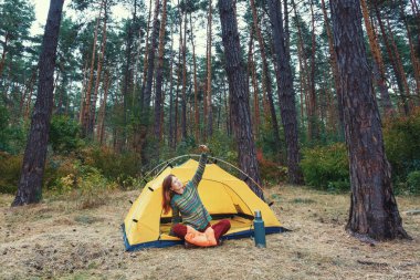 Genç kızıl saçlı kadın cep telefonuyla selfie çekiyor..