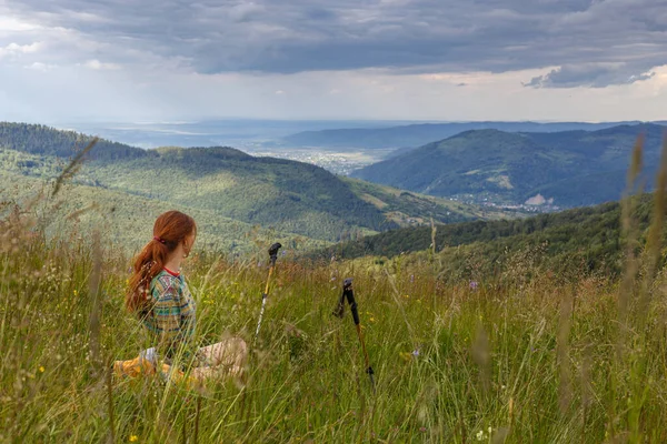 Fit mladá žena pěší turistika v horách stojí na skalnatém vrcholu hřebenu s batohem a tyčí s výhledem na alpskou krajinu — Stock fotografie