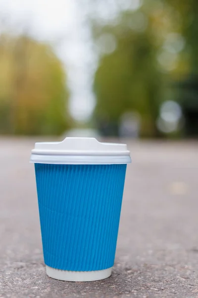 En blå kaffekopp står på asfalten i stadsparken — Stockfoto