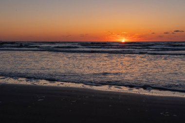 Karadeniz 'de gün batımında muhteşem bir manzara ve üzerinde muhteşem bir güneş ışığı olan turuncu gökyüzü arka plan olarak sakin dalgaların üzerinde. Sahilde muhteşem bir yaz gün batımı manzarası. Rus doğası, Soçi.