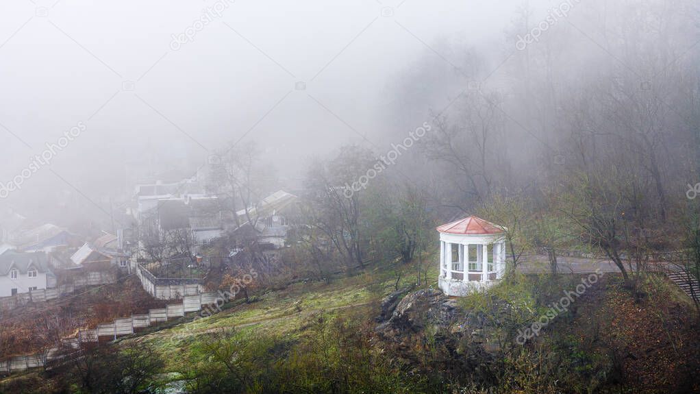 White gazebo with red roof in a dense fog. Concept of solitude and serenity. Mystical and mysterious landscape