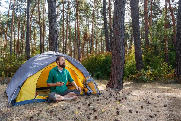 Bonito jovem barbudo ouvindo música em fones de ouvido no acampamento ao ar livre — Fotografia de Stock