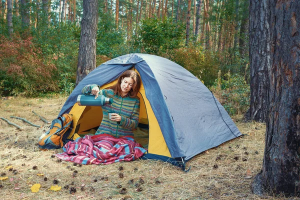 Menina nova derramando chá na xícara de garrafa térmica ao ar livre na barraca de acampamento — Fotografia de Stock