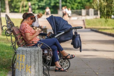 Zhitomyr, Ukrayna - 10 Temmuz 2018: Kadın bebeğiyle bankta yürüyor ve telefonla oynuyor
