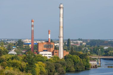 Red bricked thermal power station with tall exhaust pipes in trees