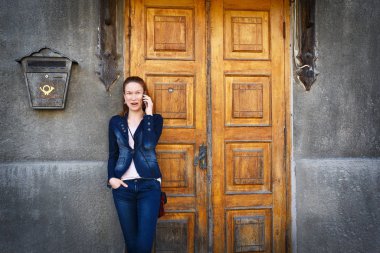 Excited surprised young woman over old wooden door and talking on phone