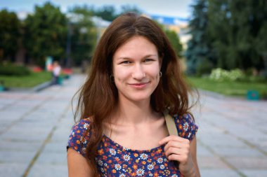 Şehir meydanında dikilen, gülümseyen genç bir kadının yakın çekimi.