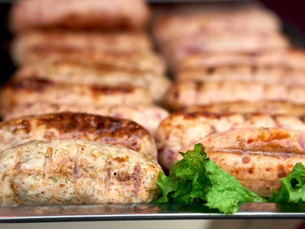 Rows of freshly grilled chicken meat sausages on tray with fresh lettuce at street food festival — 스톡 사진