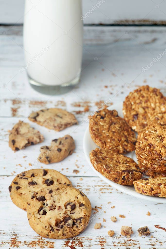 White plate with granola wholegrain cookies and glass cup of milk on wooden surface.
