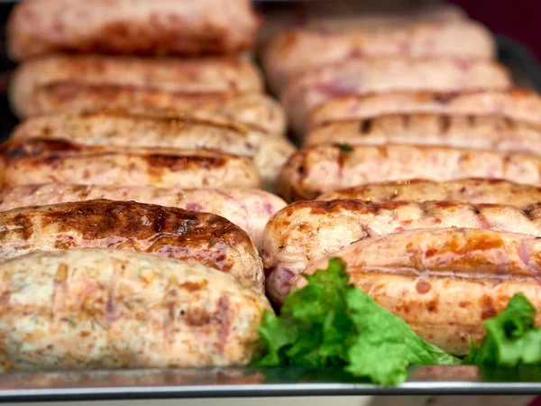 Rows of freshly grilled chicken meat sausages on tray with fresh lettuce — 스톡 사진