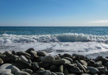 Güneşli bir günde ön planda çakıl taşlarıyla deniz sörfü