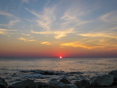 Sahilde şafak sökerken ön planda taşlar ve çakıl taşlarıyla, 