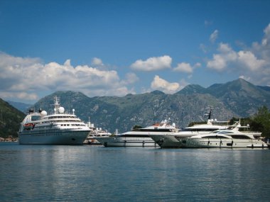 Karadağ 'ın Kotor limanında beyaz gemi ve yatlar, dağların arka planına ve mavi gökyüzüne karşı