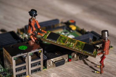 Direnişçilerin el yapımı iki küçük insan figürü SODIMM bellek modülünün modern engebeli bilgisayar panosuna kurulmasına yardımcı oluyor.