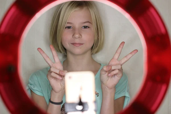 Nane rengi tişörtlü şirin blogger kızı internette takipçileri için kanalda video çekiyor. Zaferin sembolü. Yuvarlak Led Circle Lambası ve akıllı telefon