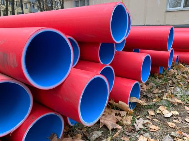 Birçok istiflenmiş kırmızı ve mavi pvc plastik sıhhi tesisat boruları açık havada yatıyordu.