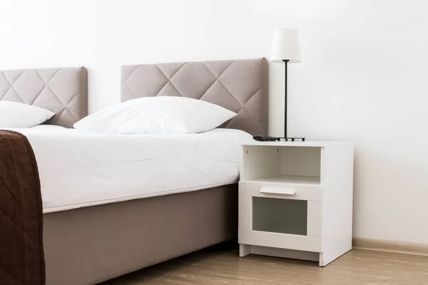 Europeiska ljusa sovrum interiör med brun, beige mysig säng och vitt linne, och ett vitt nattduksbord nära — Stockfoto