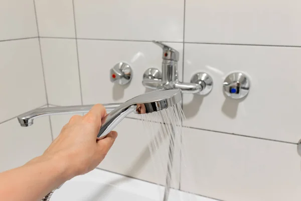 Cabezal de ducha de mano de las mujeres con agua de vertido en el baño doméstico, grifo de ducha, grifo en el bacground — Foto de Stock