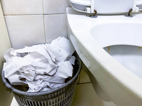 Cubo de basura desbordante, cubo de basura lleno de papel higiénico usado cerca del inodoro en un baño público — Foto de Stock