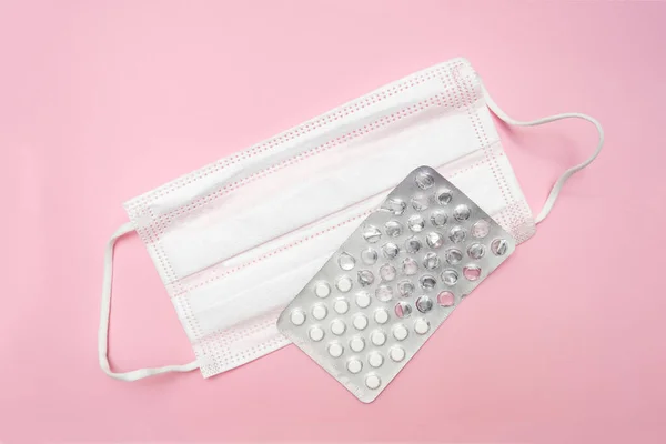 Medical surgical textyle filter protective mask and used blister of tablets on pink background, illness and flu defense