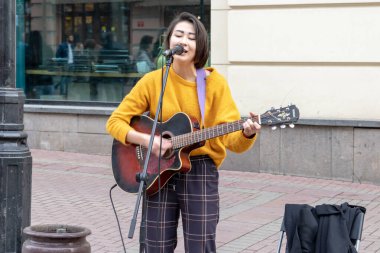 Moskova, Rusya - 19 Ekim 2019: Gitar çalan ve para kazanmak için şarkı söyleyen genç bayan sokak müzisyeni