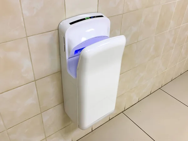 White modern hand dryer with blue lighting hanging on the wall in a public toilet, WC