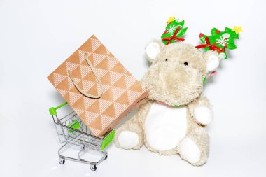 Teddy Hippo, Noel ağacı süslemeli ve alışveriş arabalı yumuşak oyuncak, içinde beyaz arka planda kağıt alışveriş torbası olan tramvay.