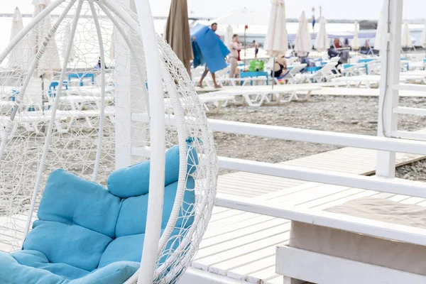 Modern design white luxury hanging rattan wicker chair egg form with cozy blue pillows inside on the beach