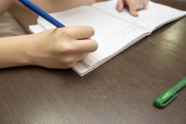 Uczeń odrabiający lekcje, pisze w notatniku z długopisem, ręce do góry — Zdjęcie stockowe
