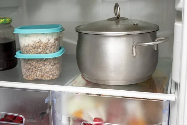 Prateleiras de um refrigerador de geladeira aberto com comida diferente, comida cozida em panela e recipiente de plástico — Fotografia de Stock