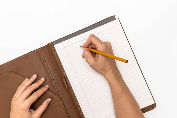 Les mains de la femme tenant un carnet avec couverture en cuir et un crayon jaune et l'écriture, vue rapprochée du dessus — Photo