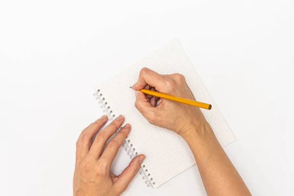 Les mains de la femme tenant un cahier et un crayon jaune et écrivant, vue rapprochée du dessus — Photo