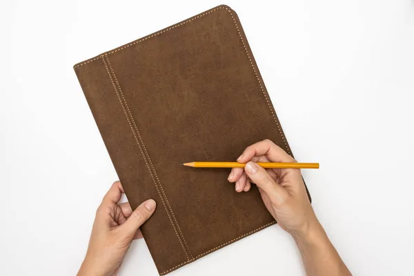 Organisateur de carnet de notes de travail avec couverture en cuir et mains de femme d'affaires tenant un crayon jaune sur fond blanc, vue de dessus — Photo