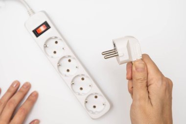 Ana eklenti prizini tutan bir el ve birçok soketle ana eklenti kablosuna sokmaya çalışıyor.