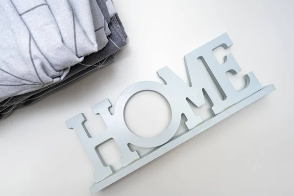 Ein Stapel gemütlicher Heimtextilien in Grautönen der Bettwäsche, Bettwäsche mit dem Hinweisschild nach Hause in der Nähe — Stockfoto