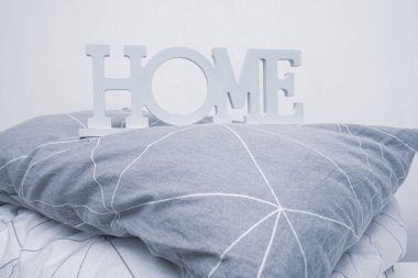 Gri, yastık ve battaniyenin gölgelerinde ev tabelası olan yumuşak yatak yığını, tekstil konsepti