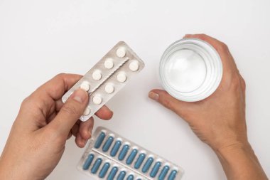Hap alan bir kadın, beyaz haplar, kapsüller ve bir bardak su tutan bir kadın eli beyaz masa, sağlık ve grip tedavi konsepti