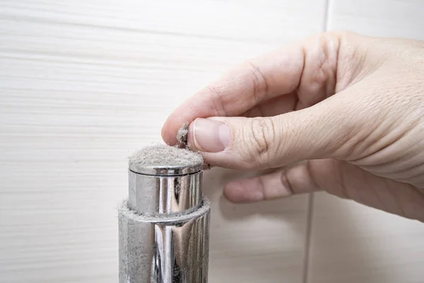 Dedos sosteniendo un pedazo de polvo de cromado en el cuarto de baño, el concepto de casa polvorienta — Foto de Stock