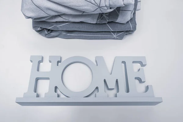 Ein Stapel gemütlicher Heimtextilien in Grautönen der Bettwäsche, Bettwäsche mit dem Hinweisschild nach Hause in der Nähe — Stockfoto