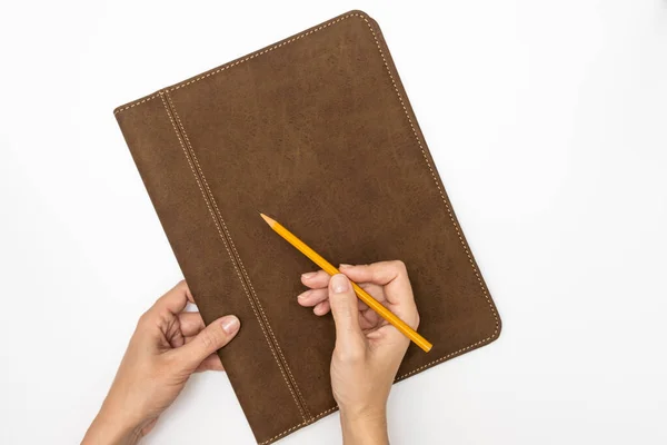 Organisateur de carnet de notes de travail avec couverture en cuir et mains de femme d'affaires tenant un crayon jaune sur fond blanc, vue de dessus — Photo
