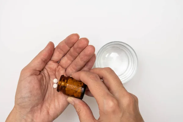 Mujer tomando píldoras, manos femeninas con píldoras de botella de vidrio y un vaso de agua en la mesa blanca — Foto de Stock