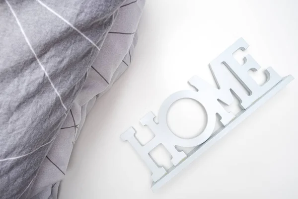 Una pila di biancheria da letto morbida accogliente nei toni del grigio, cuscini e coperta con un segno di casa, concetto di tessile per la casa — Foto Stock